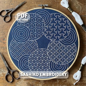 May include: A blue fabric embroidery hoop with white Sashiko stitching in various geometric patterns. The text "PDF PATTERN" and "SASHIKO EMBROIDERY" are visible. Two pairs of small scissors and white thread spools are also in the image.