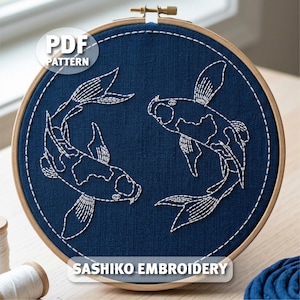 May include: A navy blue fabric embroidery hoop with a Sashiko design of two koi carp. The fish are outlined in white thread, with details of the fish's scales and fins. The text "PDF PATTERN" and "SASHIKO EMBROIDERY" are displayed on the image.