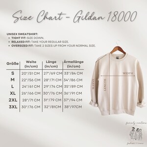 May include: A beige Gildan 18000 unisex sweatshirt displayed on a wooden hanger. The image includes a size chart with measurements in inches and centimeters for width, length, and sleeve length. Text on the image includes "Size Chart - Gildan 18000".