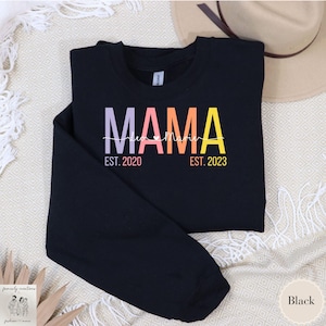 Puede incluir: Sudadera negra con el texto "MAMA" en colores arcoíris con un corazón y el texto "EST. 2020" y "EST. 2023" debajo.