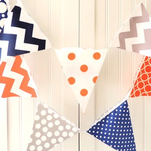 May include: A white bunting with orange, gray, and blue triangle flags. The flags have different patterns, including polka dots, zigzags, and circles.