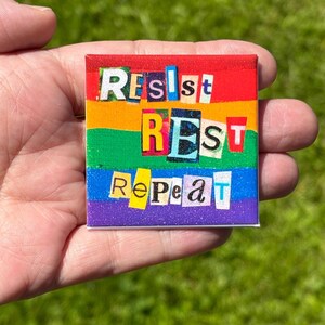 Puede incluir: Un pin cuadrado con un fondo de colores del arcoíris con franjas horizontales en rojo, naranja, amarillo, verde, azul y morado. El texto "RESIST REST REPEAT" se muestra en estilo collage con letras recortadas de diversas fuentes.