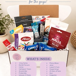 May include: A white cardboard gift box labeled FALL CARE PACKAGE for the guys! containing assorted items including Halls cough drops, Oreo cookies, Albanese gummi worms, Emergen-C, a Paper Mate pen pack, beef jerky, and other snacks and personal care items.