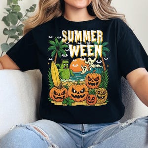May include: Black t-shirt with a colorful graphic that reads "SUMMER WEEN". The design features a beach scene with pumpkins, ghosts, palm trees, and a monster holding a surfboard. The sun is setting over the ocean.