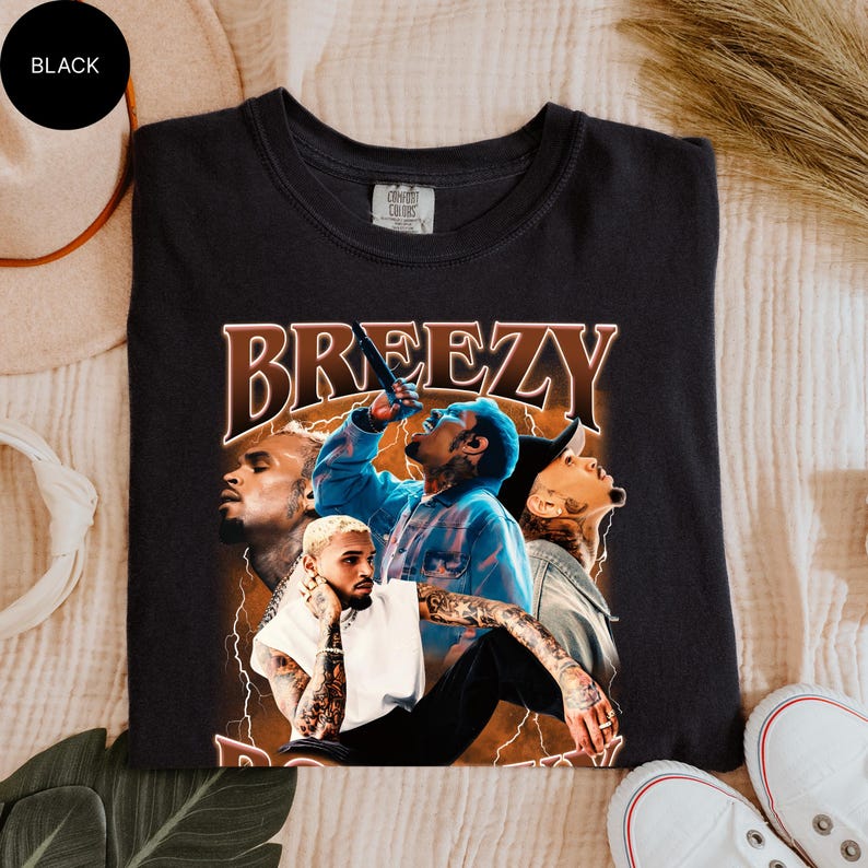 Puede incluir: Camiseta negra con un gr&aacute;fico de un cantante y la palabra "Breezy" en fuente marr&oacute;n. El gr&aacute;fico incluye im&aacute;genes del cantante en diferentes poses. La camiseta est&aacute; hecha de un material suave.