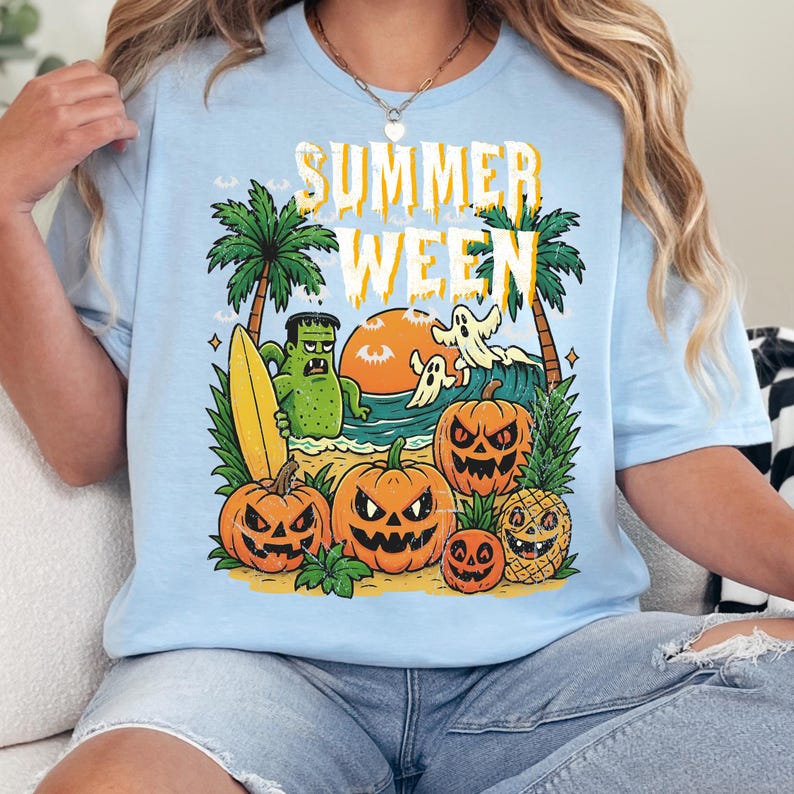 May include: Light blue t-shirt with a colorful graphic that says "SUMMER WEEN". The design features a beach scene with pumpkins, palm trees, a monster holding a surfboard, and ghosts. A fun, festive tee for Halloween.