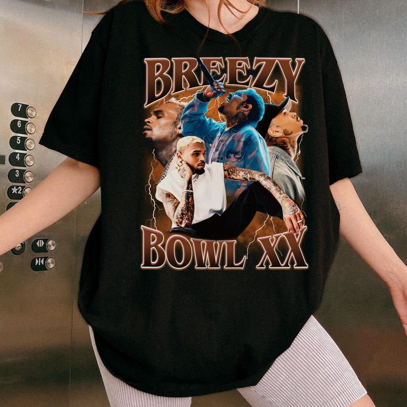 Puede incluir: Camiseta negra con un dise&ntilde;o gr&aacute;fico que dice "BREEZY BOWL XX". El dise&ntilde;o presenta m&uacute;ltiples im&aacute;genes de una persona en diferentes poses, utilizando colores azules y marrones. Es una prenda informal.