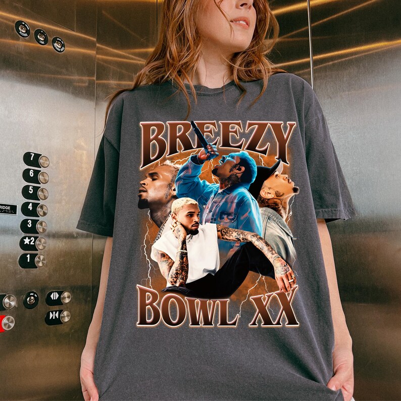 Puede incluir: Camiseta gris oscuro con un dise&ntilde;o gr&aacute;fico. La palabra "BREEZY" en letras marrones est&aacute; sobre un collage de im&aacute;genes. Las im&aacute;genes incluyen una persona con una camisa azul y otros retratos. El texto "BOWL XX" est&aacute; debajo.