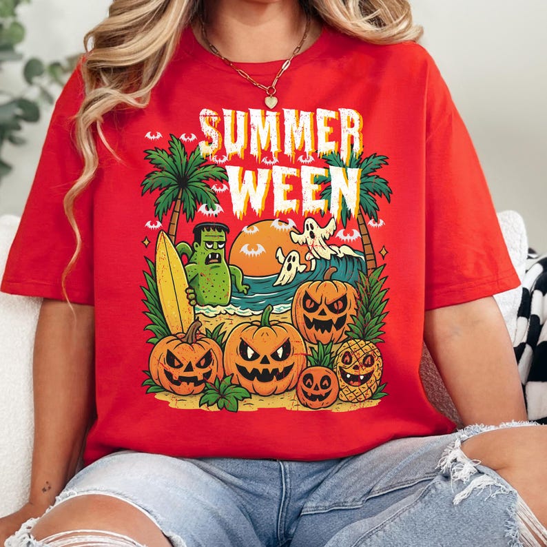 May include: Red t-shirt with a graphic design featuring the text "SUMMER WEEN". The design includes palm trees, a Frankenstein monster with a surfboard, ghosts, pumpkins, and a pineapple with a jack-o'-lantern face. The shirt is a casual wear item.