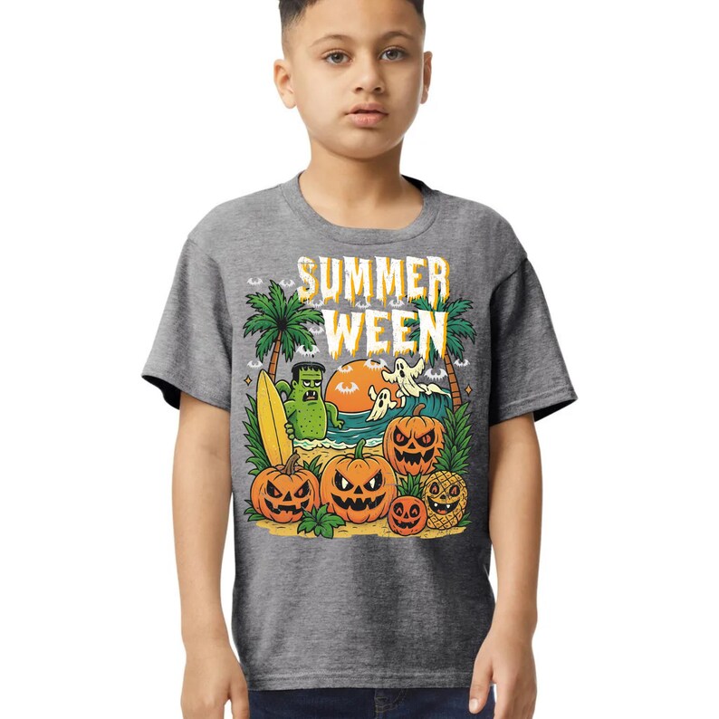 May include: A gray t-shirt featuring a colorful graphic with the text "SUMMER WEEN." The design includes pumpkins, palm trees, a monster, ghosts, and a surfboard, creating a fun, seasonal theme.