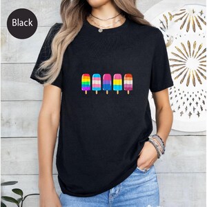 May include: Black t-shirt featuring a row of five colorful popsicle illustrations. Each popsicle has a different design, including rainbow stripes, pink and white stripes, and blue and pink stripes. The shirt is a solid black color.