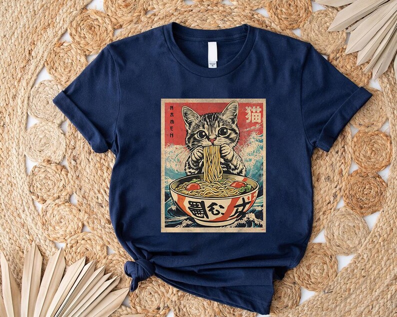 A navy blue t-shirt with a graphic design depicting a cat eating noodles from a bowl.