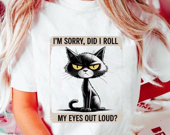 May include: White t-shirt featuring a cartoon illustration of a black cat with an angry expression and yellow eyes. The text on the shirt reads "I'M SORRY, DID I ROLL MY EYES OUT LOUD?" The cat is sitting upright.