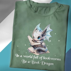 Peut inclure: Un t-shirt vert avec un dragon blanc lisant un livre. Le texte sur le t-shirt est "Dans un monde plein de vers de livres Soyez un dragon de livre".