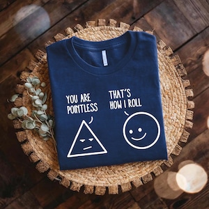 May include: Navy blue t-shirt with the text "YOU ARE POINTLESS" and "THAT'S HOW I ROLL" in white. The design includes a triangle with a frowning face and a smiling circle.