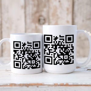 Op de afbeelding: Twee witte keramische mokken met zwarte QR-code ontwerpen. De mokken hebben een standaard handvat en een cilindrische vorm. De QR-codes zijn zwart afgedrukt op de voorkant van de mokken. De mokken zijn waarschijnlijk voor dranken.