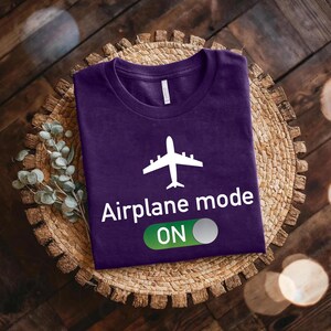 a purple t-shirt with a white airplane graphic and the text "Airplane mode ON" printed on it, placed on a woven basket or plate.
