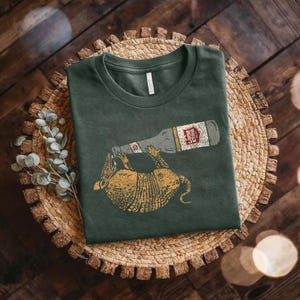 a green t-shirt with a graphic design of a bottle and a cartoon animal, possibly a dog, on it, placed on a woven basket or plate.