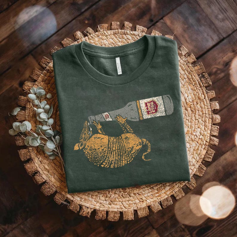 a green t-shirt with a graphic design of a bottle and a cartoon animal, possibly a dog, on it, placed on a woven basket or plate.