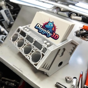 May include: A 3D printed gray engine block with a slot for holding business cards. The business cards have a logo with a blue cartoon hippopotamus and the text "Diggity3D".