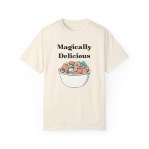 Könnte beinhalten: Ein cremefarbenes T-Shirt mit einem Aufdruck einer Schüssel mit Müsli und dem Text "Magically Delicious".