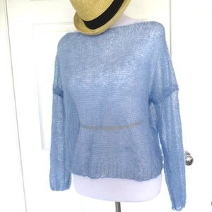 May include: A light blue, loose-fitting, knitted sweater with long sleeves. The sweater is made of a sheer, delicate fabric.