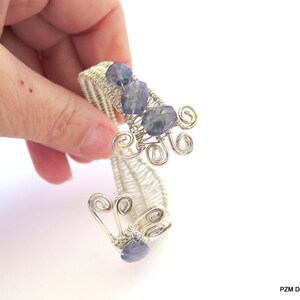 May include: Silver wire bracelet with blue gemstone accents and a delicate, intricate design. The bracelet is made with wire wrapped around the stones, creating a unique and elegant look.