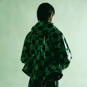 Puede incluir: Chaqueta con capucha brillante con un patr&oacute;n de cuadros negros y verdes. La chaqueta tiene una superficie brillante y reflectante y un dise&ntilde;o corto. La persona de la imagen est&aacute; de espaldas.