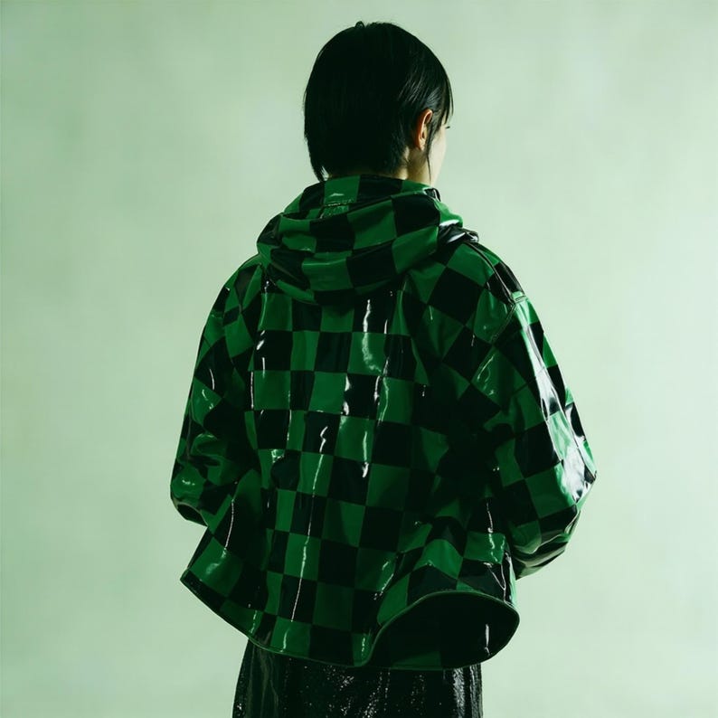 Puede incluir: Chaqueta con capucha brillante con un patr&oacute;n de cuadros negros y verdes. La chaqueta tiene una superficie brillante y reflectante y un dise&ntilde;o corto. La persona de la imagen est&aacute; de espaldas.