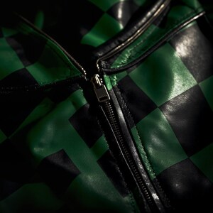 Puede incluir: Primer plano de una chaqueta a cuadros negros y verdes con cremallera plateada. La chaqueta est&aacute; hecha de un material similar al cuero y tiene un patr&oacute;n de tablero de ajedrez cl&aacute;sico. La cremallera est&aacute; cerrada.