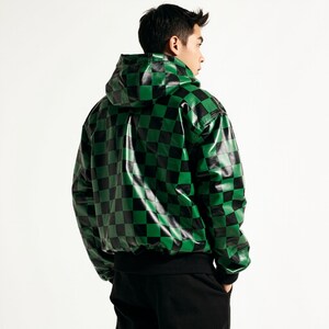 Puede incluir: Una chaqueta con capucha con un patr&oacute;n de tablero de ajedrez negro y verde. La chaqueta tiene un dobladillo y pu&ntilde;os de canal&eacute; negros. El material parece ser brillante, posiblemente polipiel. La chaqueta se lleva sobre pantalones negros.