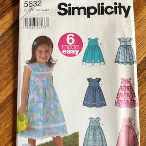 May include: A Simplicity 5632 sewing pattern envelope for a child's dress in size A 1/2, 1, 2, 3, 4. The front features a photo of a child wearing a blue floral dress with white trim, alongside illustrations of six dress variations in different colors.