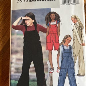 May include: Butterick sewing pattern 3958 featuring illustrations of overalls in three styles. One pair is solid black with side buttons, one is red shorts-style overalls, and one is blue denim with a white star pattern and cargo pockets.