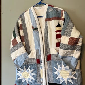 May include: A white ceramic mug with a black handle and the text "But First, Coffee" in a bold, black font. The mug is set against a blurred background, suggesting a cozy setting.