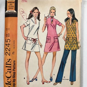 May include: A vintage McCall's 2245 sewing pattern envelope featuring illustrations of three outfits: a white dress, a pink dress, and a yellow patterned tunic with blue pants. The envelope includes text, a measuring tape at the top, and size 12.