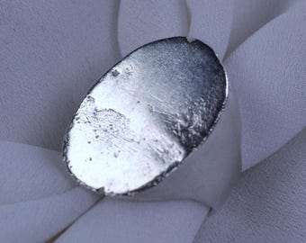 May include: A silver oval ring with a smooth, slightly textured surface.
