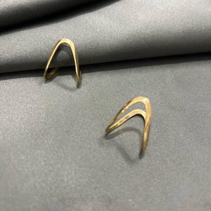 May include: Two gold-colored rings with a unique open-arch design. The rings are made of a smooth metal and have a simple, minimalist style.