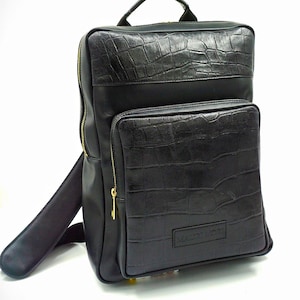 May include: Black leather backpack with a crocodile embossed design. The backpack has a large main compartment and a smaller front pocket. The zipper pulls are gold coloured. The backpack has a brand label that says "MARYVON".
