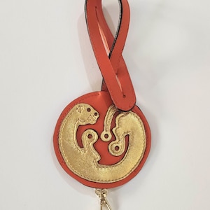 A beautiful keychain made of orange genuine leather with the symbol of Mauri Mori design on the front and the brand logo on the back