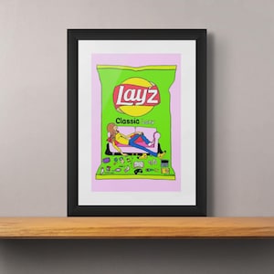 May include: A framed print of a green Lay's potato chip bag with a person relaxing on a couch inside. The bag says "Lay's Classic Lay's" and has a pink background.
