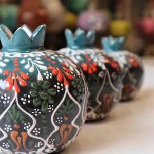 May include: Three ceramic pomegranate ornaments with intricate hand-painted designs in shades of green, orange, white, and black.