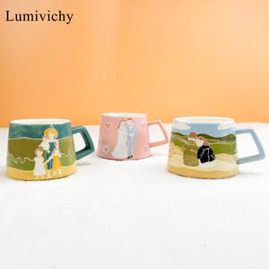 Puede incluir: Tres tazas de cer&aacute;mica con dise&ntilde;os &uacute;nicos. Una taza es verde azulado con una ilustraci&oacute;n familiar, otra es rosa con una pareja, y la &uacute;ltima es azul claro con una pareja. Cada taza tiene un asa cuadrada.