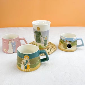 Puede incluir: Cuatro tazas de cer&aacute;mica con ilustraciones de tem&aacute;tica familiar. Una taza rosa presenta una pareja de bodas, mientras que otras representan a padres e hijos. Las tazas tienen varios colores de asa y est&aacute;n sobre una superficie blanca.