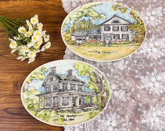 May include: Two oval decorative plates with hand-painted house portraits. One plate features a white house with the text "The Lowes". The other plate shows a house with the text "The Stanleys Est. 1984". Both plates have a colorful landscape.