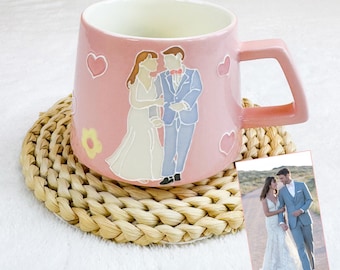 May include: Pink ceramic mug with a square handle, featuring a wedding couple illustration and heart and flower accents. The mug sits on a woven coaster, with a small photo of the couple. The mug is a unique gift idea.