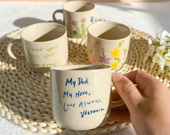 May include: Four beige ceramic mugs. One mug has the text "My Dad My Hero, Love Always, Victoria" in blue. Another mug has the text "forever your little girl Love Kirstyn". The other two mugs have floral designs in various colors.