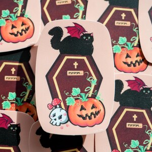 Vinyl Sticker - Spooky Vampire Cat Sitting on a Coffin Next to a Skull and Pumpkin