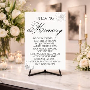 Op de afbeelding: Een wit rechthoekig bord op een zwarte ezelstandaard met de zwarte tekst IN LOVING Memory gevolgd door een gedicht over herinnering. Het bord is versierd met eenvoudige zwarte lijntekeningen van bloemen in de rechterboven- en linkerbenedenhoek.