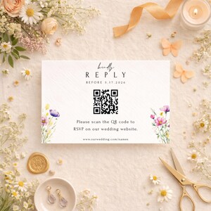 May include: A white RSVP card with floral accents and the text "kindly REPLY BEFORE 5.17.2026." A QR code is featured, with the prompt to RSVP on the wedding website. The card is surrounded by flowers and decorative elements.