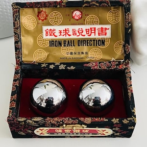 Può includere: Una scatola nera e oro con due sfere di ferro lucide. La scatola ha un interno rosso e un'etichetta dorata con testo cinese e la scritta inglese "IRON BALL DIRECTION". Prodotto in Cina.